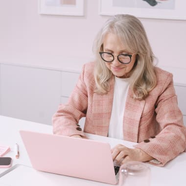 an elderly woman in a pink suit typing on a pink computer on a pink computer